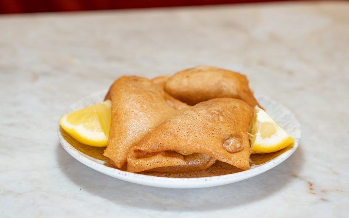 Deux briques tunisiennes frites servies dans une assiette avec des quartiers de citron
