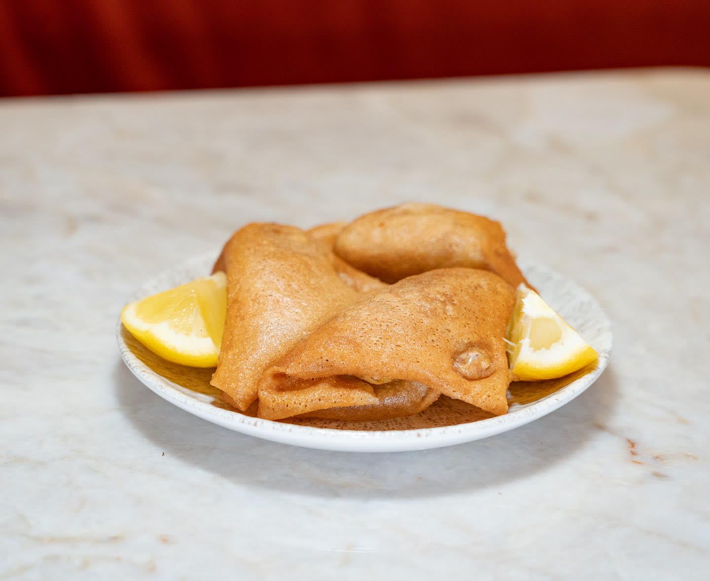 Deux briques tunisiennes frites servies dans une assiette avec des quartiers de citron