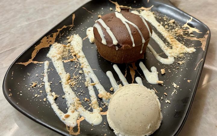 Un dessert au chocolat avec une boule de glace et un coulis blanc sur une assiette noire