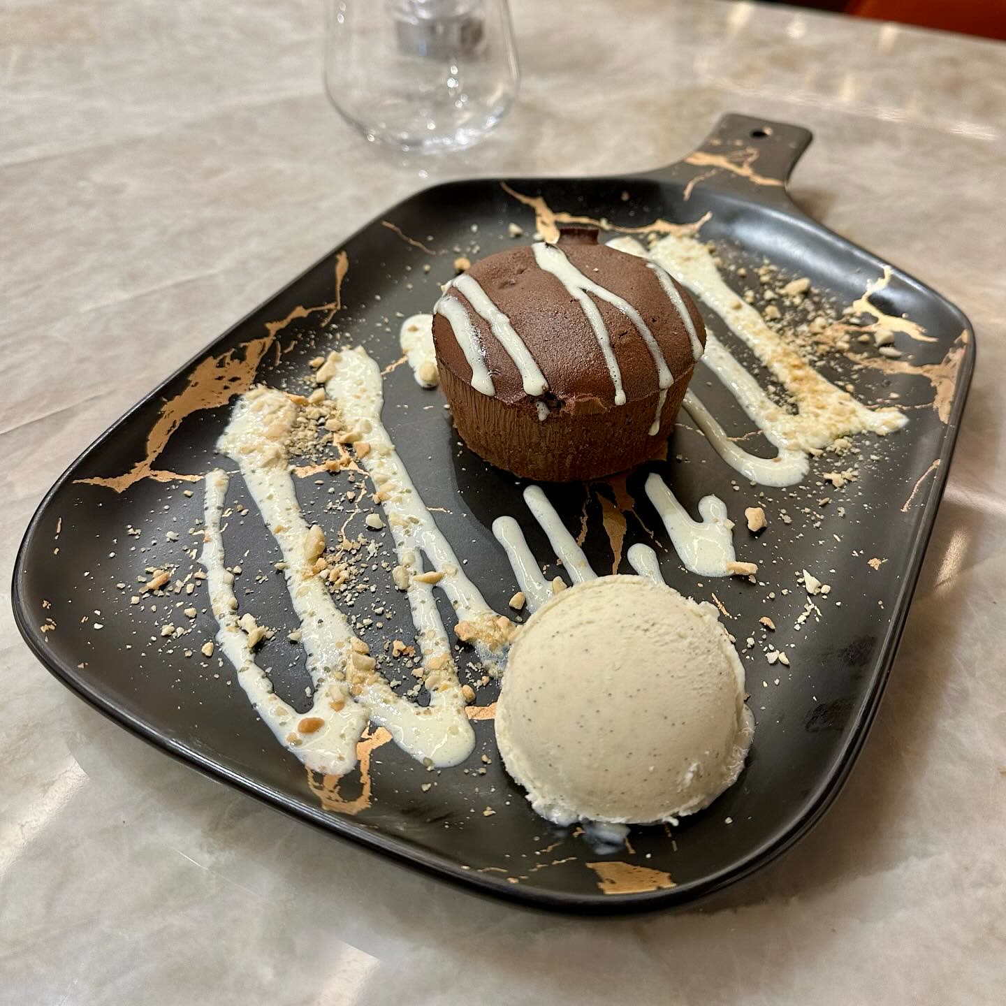 Un dessert au chocolat avec une boule de glace et un coulis blanc sur une assiette noire