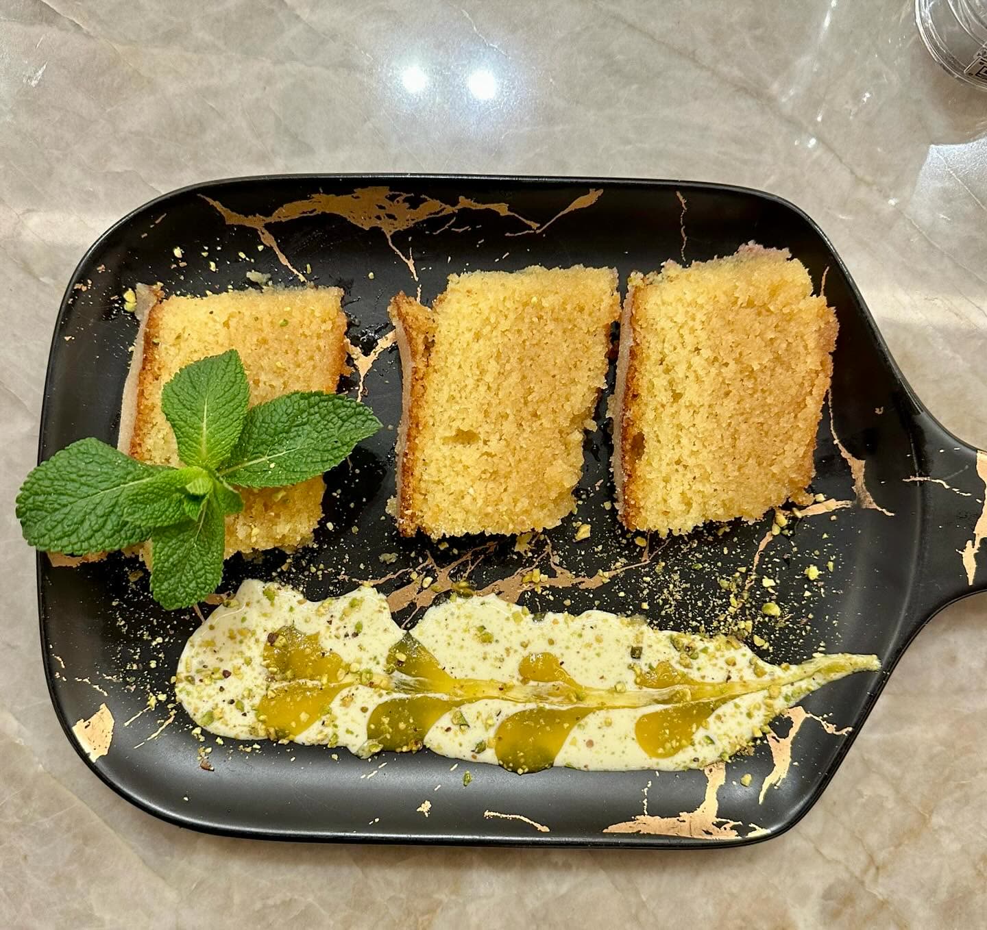 Trois tranches de cake moelleux servies sur une assiette noire avec une sauce crémeuse et de la menthe fraîche
