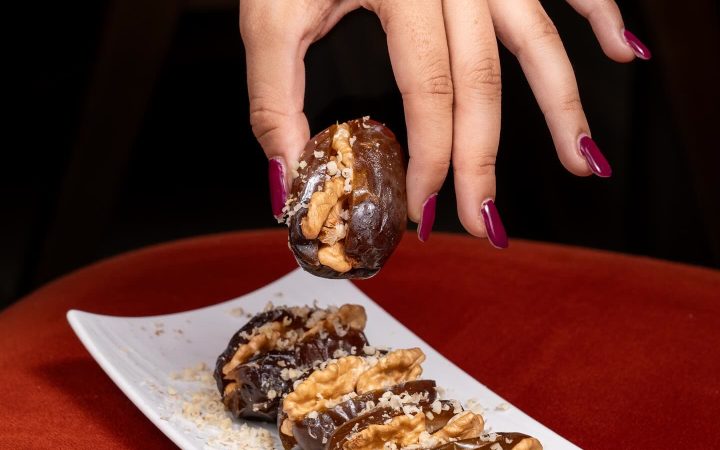 Une main présente une datte fourrée aux noix au-dessus d'une assiette de dattes similaires