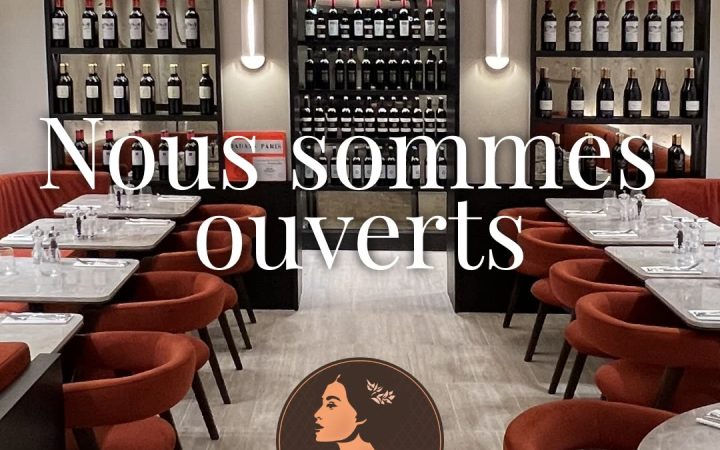 Vue de l'intérieur du restaurant montrant des étagères de bouteilles de vin et des tables dressées avec un texte indiquant l'ouverture