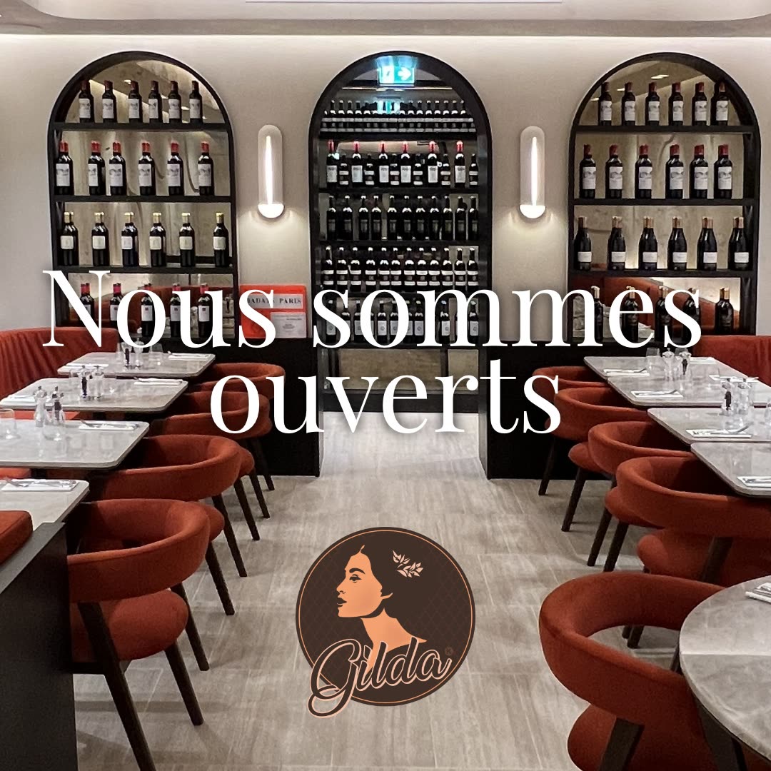 Vue de l'intérieur du restaurant montrant des étagères de bouteilles de vin et des tables dressées avec un texte indiquant l'ouverture
