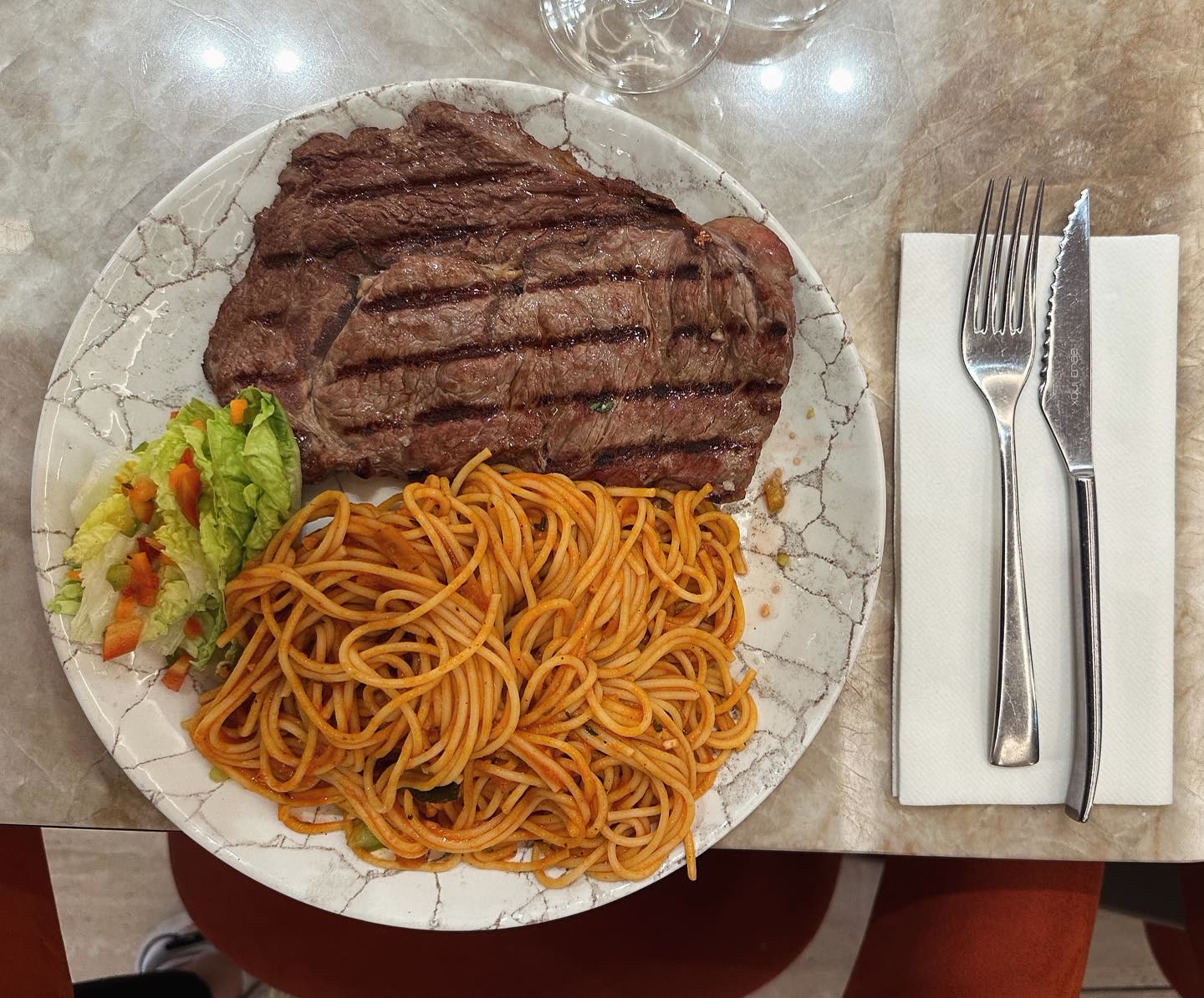 Une assiette composée d'un steak grillé et de spaghettis à la sauce tomate avec une petite salade