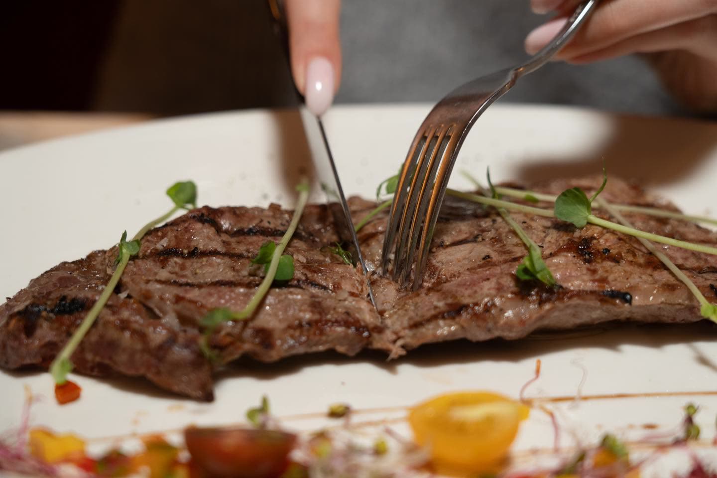 Une personne découpe une pièce de viande grillée sur une assiette blanche avec un couteau et une fourchette