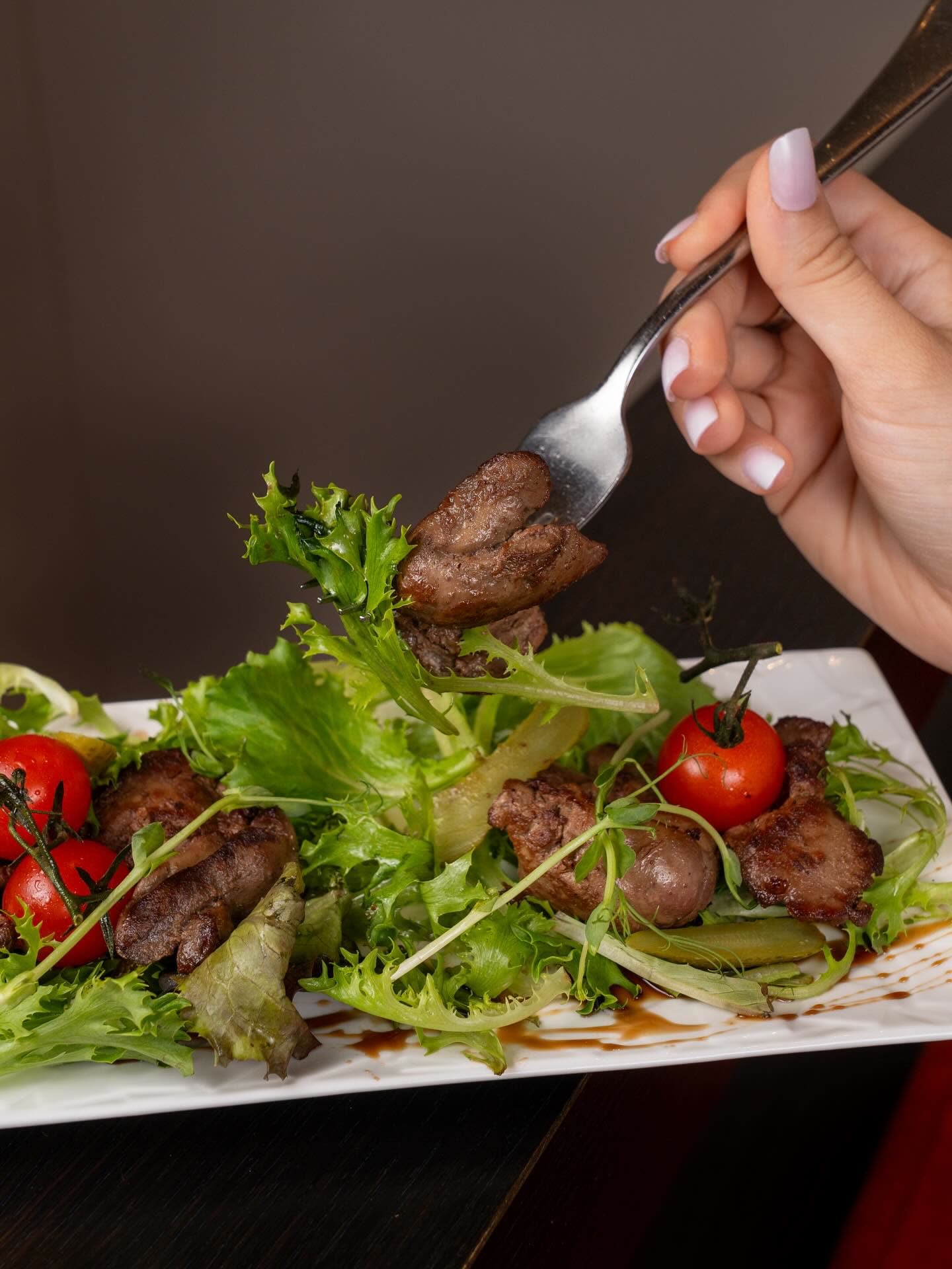 Une main utilise une fourchette pour piquer un morceau de viande sur une salade composée avec des tomates cerises