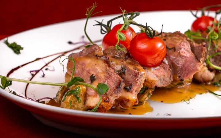 Des morceaux de viande cuisinés avec des tomates cerises et des herbes sur une assiette blanche