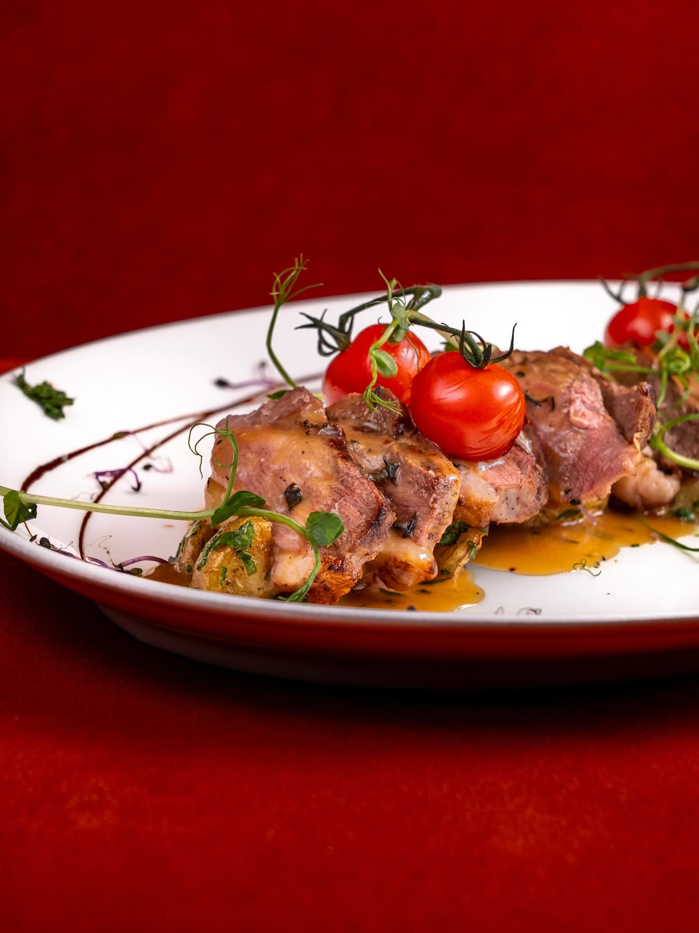 Des morceaux de viande cuisinés avec des tomates cerises et des herbes sur une assiette blanche