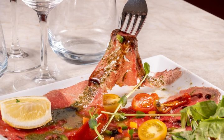 Une personne utilise une fourchette pour soulever une tranche de viande rosée sur une assiette garnie de tomates et de salade