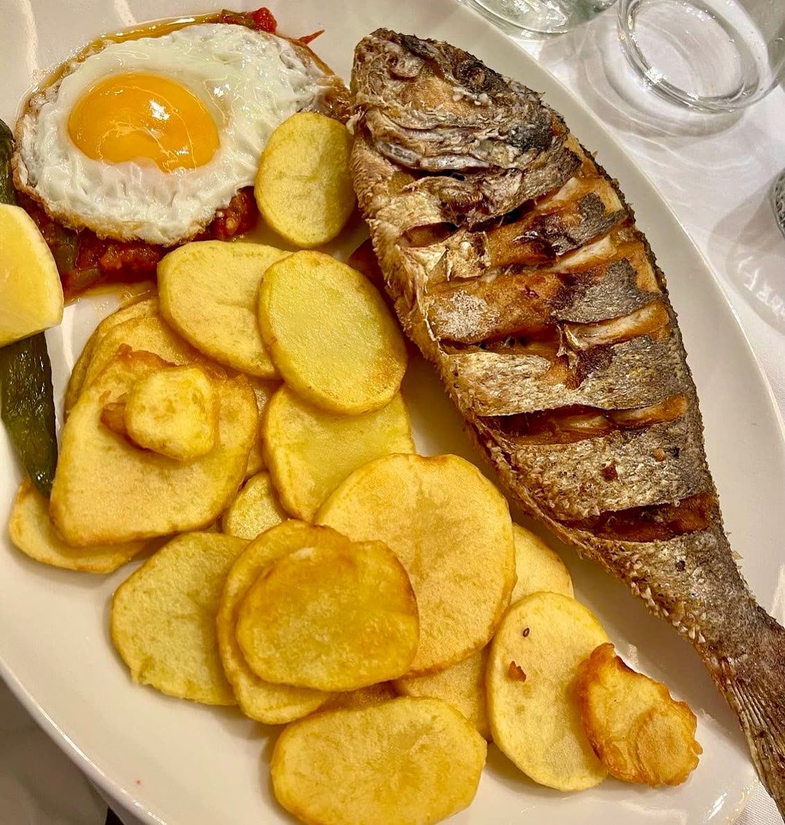 Un poisson entier frit servi avec des rondelles de pommes de terre et un œuf au plat