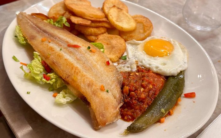 Un filet de poisson frit servi avec des pommes de terre, un œuf au plat et une sauce tomate