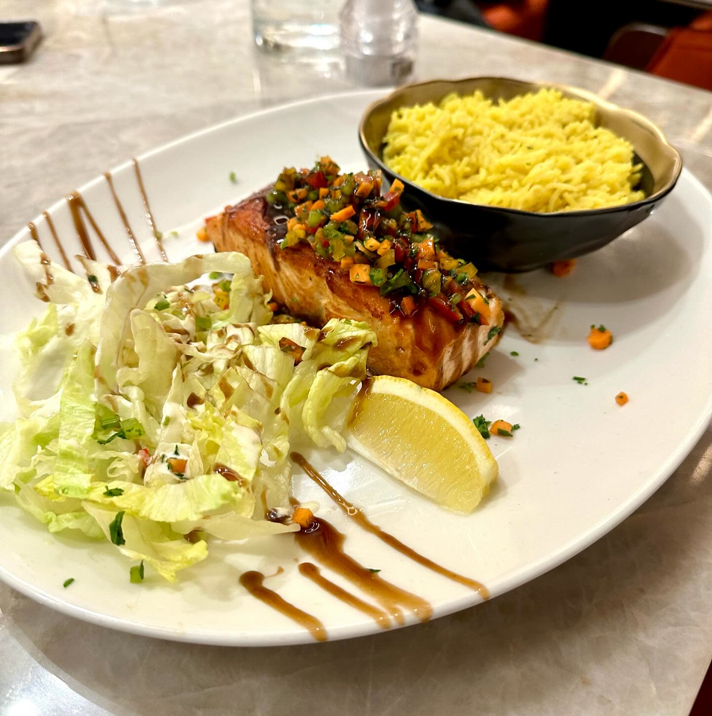 Un pavé de saumon grillé accompagné de riz jaune et d'une salade verte sur une assiette blanche