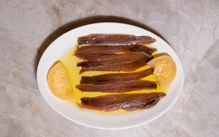 Filets de poissons marinés dans l'huile avec des quartiers de citron sur une assiette blanche