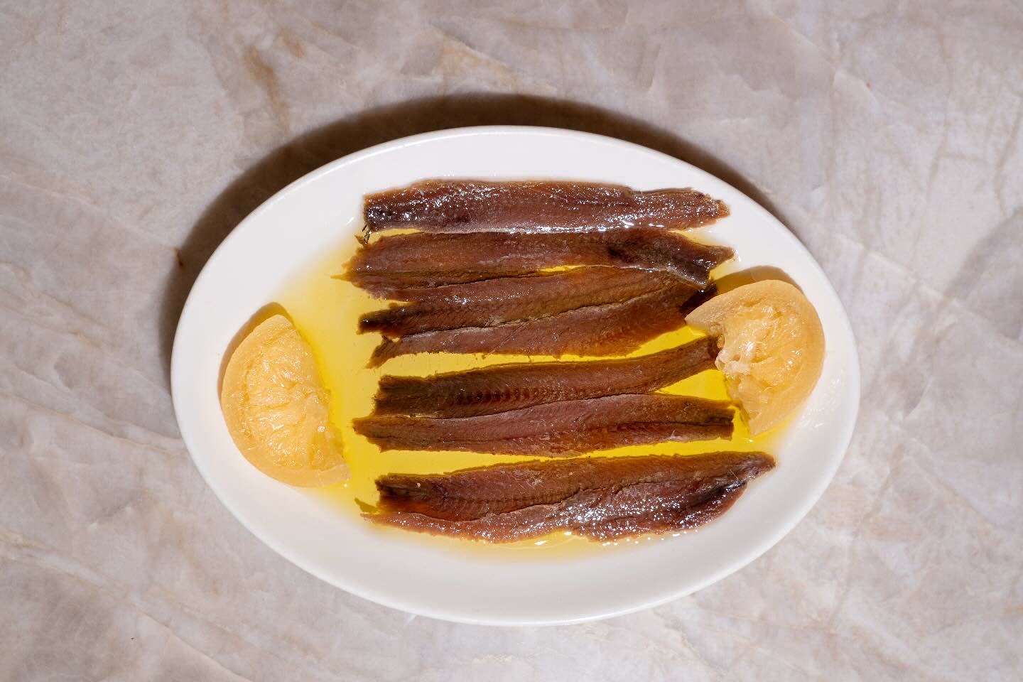 Filets de poissons marinés dans l'huile avec des quartiers de citron sur une assiette blanche