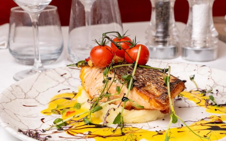 Un filet de saumon grillé servi avec des tomates cerises et une sauce jaune sur une assiette décorée