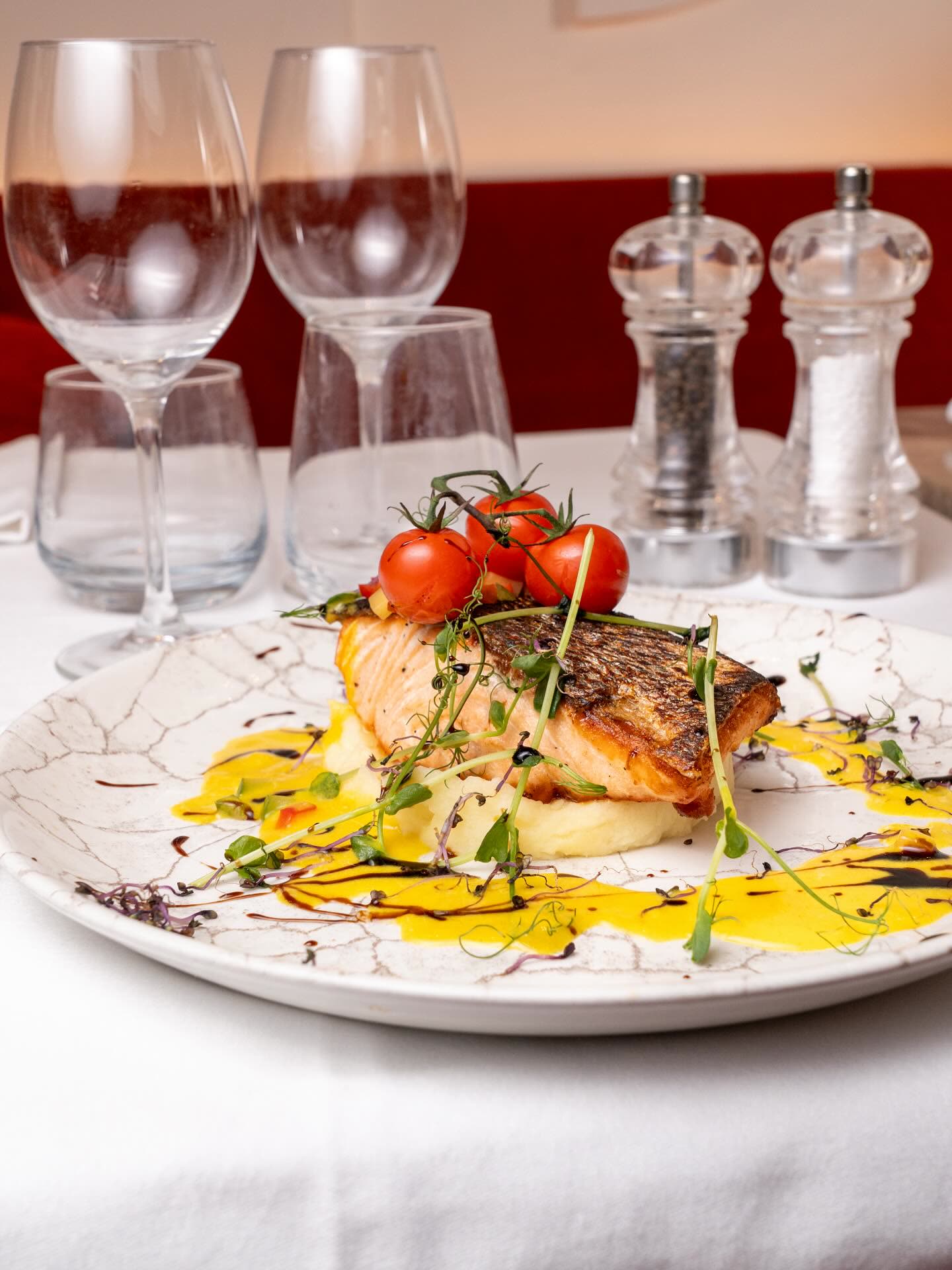Un filet de saumon grillé servi avec des tomates cerises et une sauce jaune sur une assiette décorée
