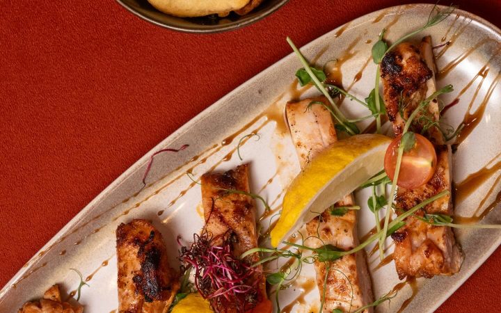 Un plat de poisson grillé accompagné de quartiers de citron et de tomates cerises sur une assiette allongée