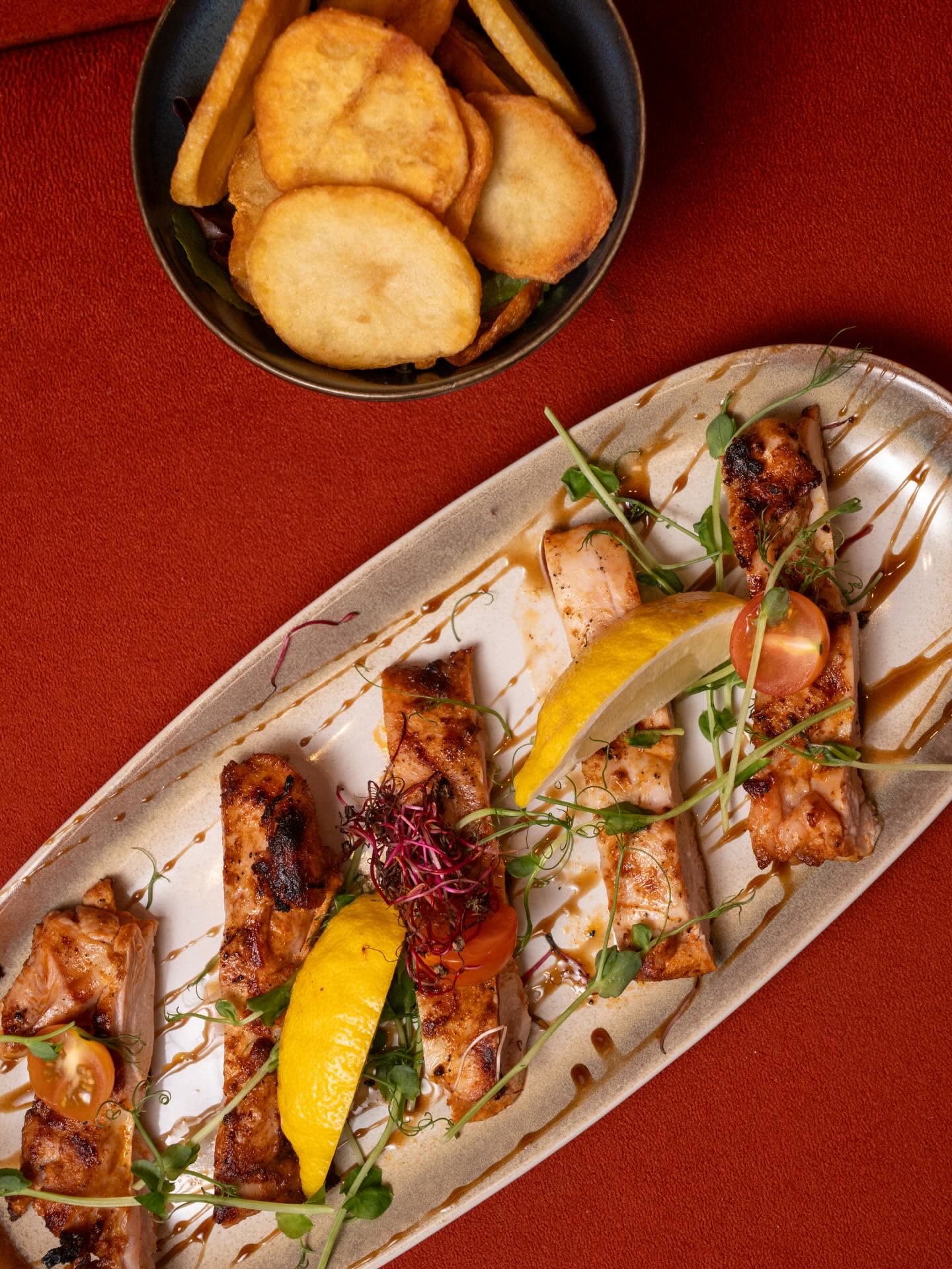 Un plat de poisson grillé accompagné de quartiers de citron et de tomates cerises sur une assiette allongée