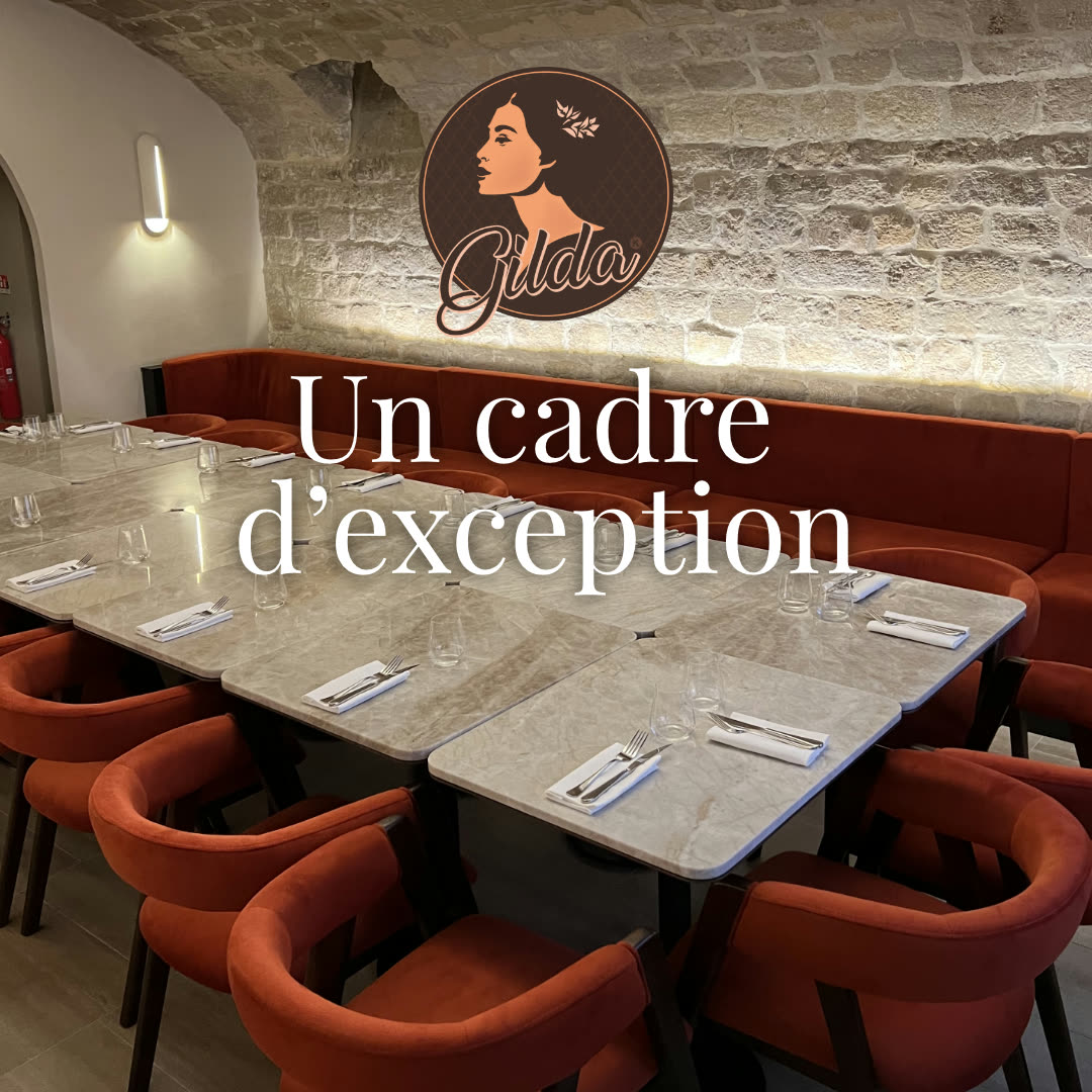 Une salle de restaurant avec des tables dressées, des chaises rouges et un logo sur un mur en pierre