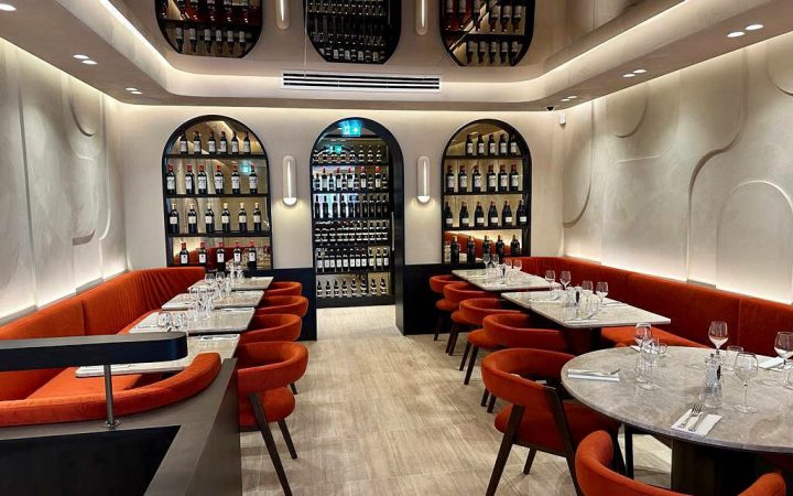 L'intérieur d'un restaurant avec des banquettes orange et des étagères de bouteilles de vin encastrées dans les murs
