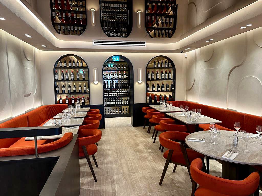 L'intérieur d'un restaurant avec des banquettes orange et des étagères de bouteilles de vin encastrées dans les murs