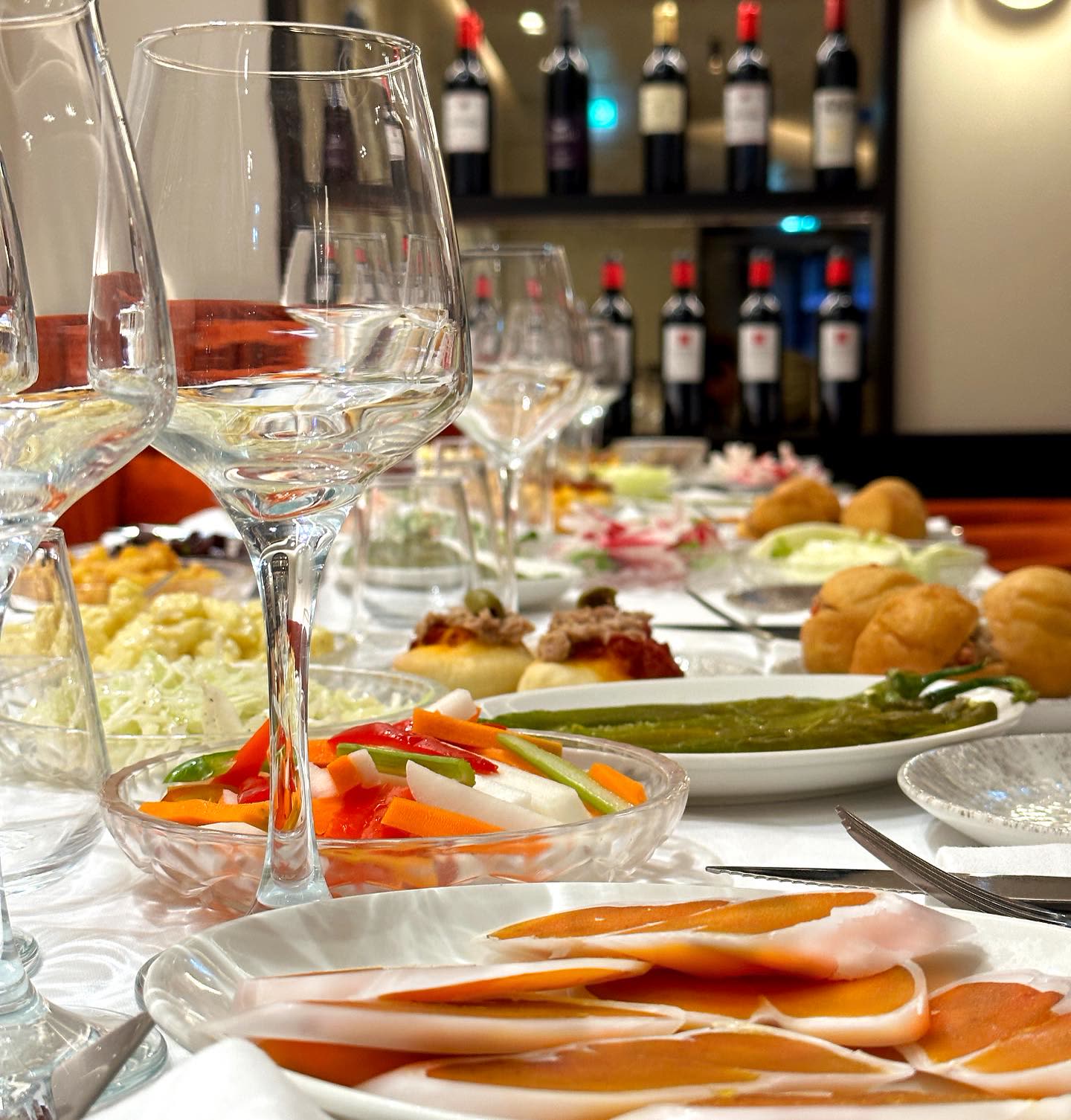 Une table dressée avec divers plats de kemia, des verres à vin et des assiettes de crudités