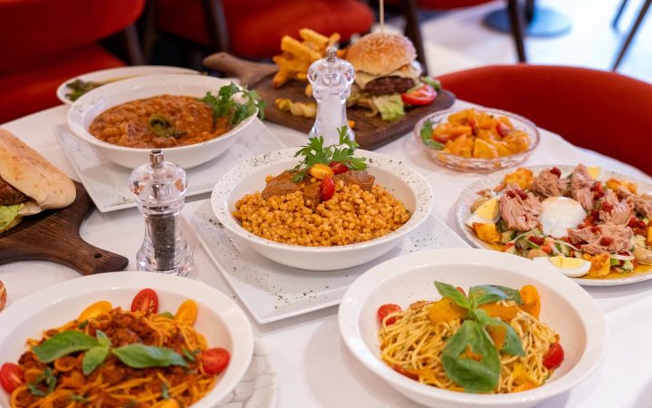 Une table garnie de divers plats tunisiens et internationaux comme du couscous, des pâtes et un burger