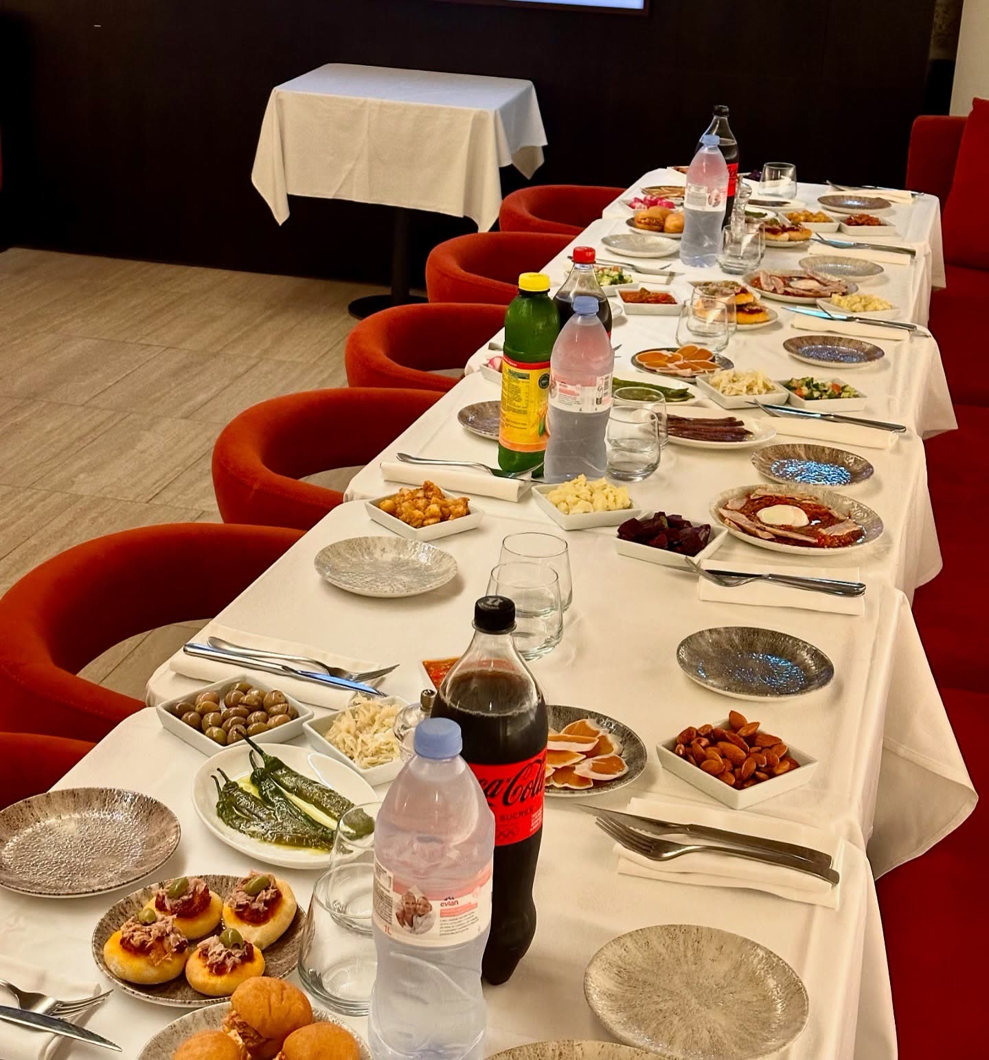 Une table longue dressée avec de nombreux petits plats, des boissons et des couverts pour un repas de groupe