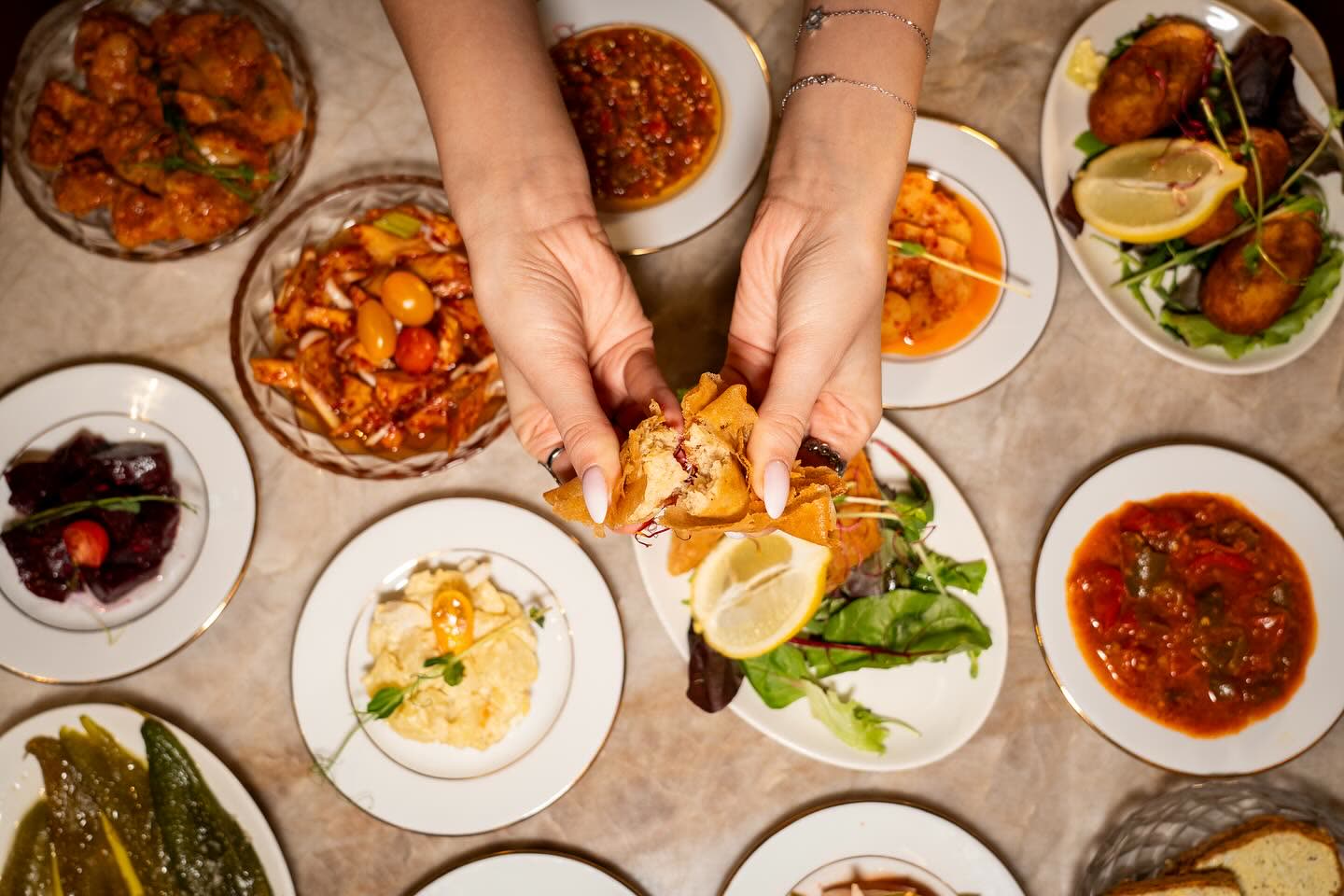 Une vue de dessus d'une table garnie de nombreux plats de cuisine tunisienne avec des mains tenant un morceau de pain