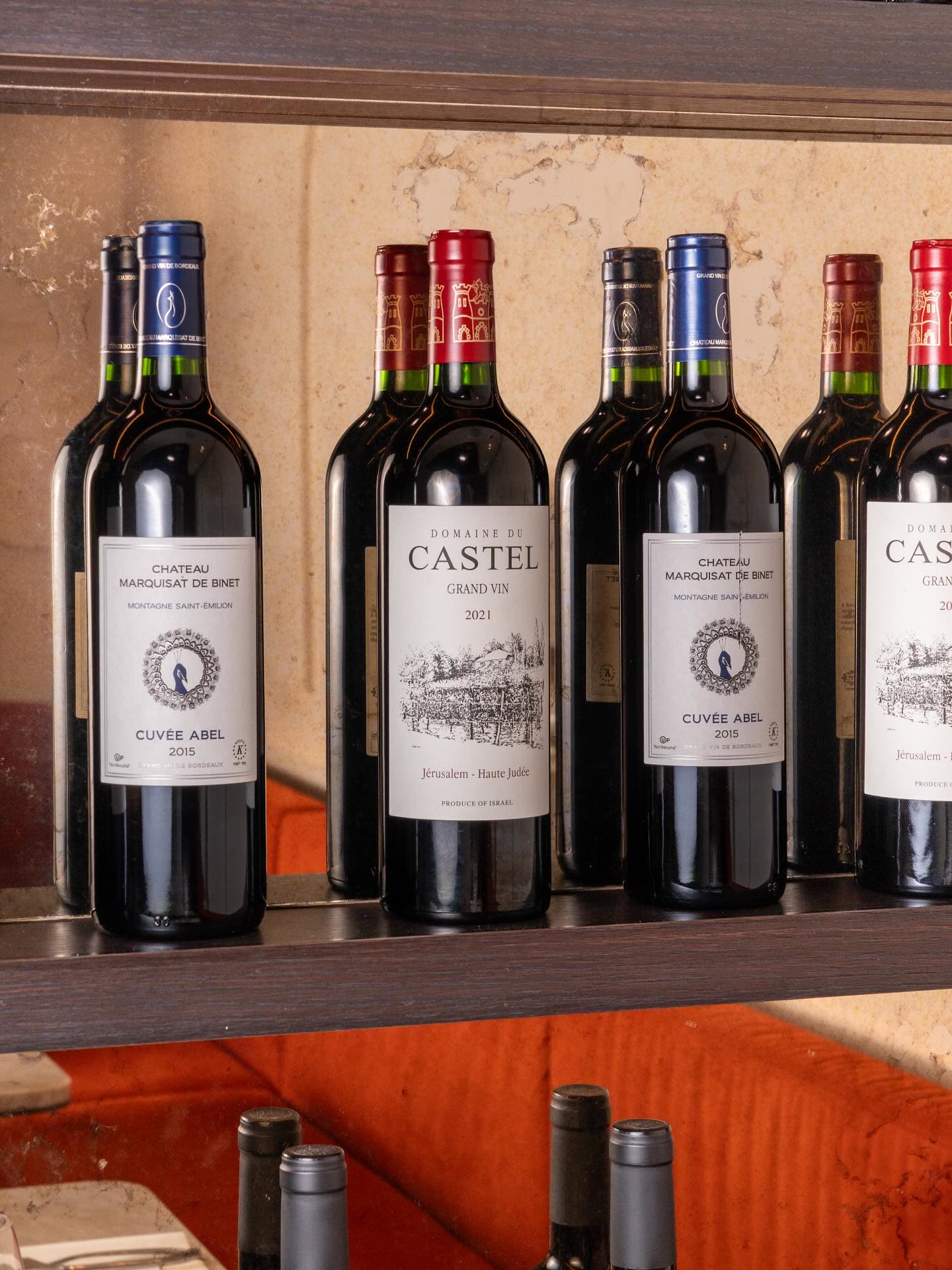 Plusieurs bouteilles de vin rouge sont alignées sur une étagère dans un restaurant